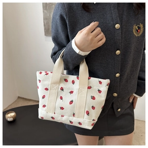 Detail of strawberry print corduroy tote bag held by a model in casual outfit