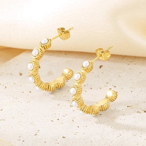 Detail view of gold C-shape stud earrings with pearls on a textured stone base