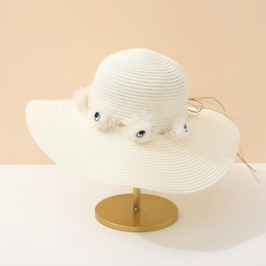 Détail de chapeau en paille crème avec pompons blancs et broderie d'yeux