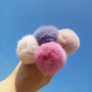 Detail of soft faux fur pom poms in pink and cream held against a blue sky