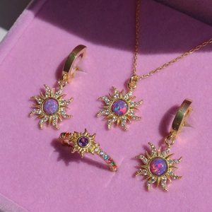 Gold sunburst jewelry set with purple opal pendants and rings on pink velvet