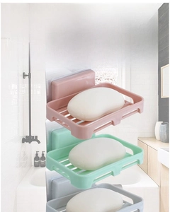 Wall-mounted soap dishes in pink, green, and gray with drainage slots in a bathroom