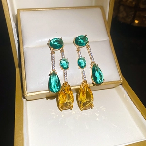 Détail de boucles d'oreilles dorées avec zircons verts et jaunes en écrin à bijoux