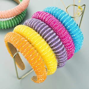 Colorful handmade beaded headbands with wide sponge padding displayed on a metal rack