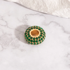 Detailed view of a gold-plated barrel bead paved with green faceted crystals for DIY jewelry