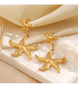 Detail shot of golden double starfish earrings on white textured base and silk fabric