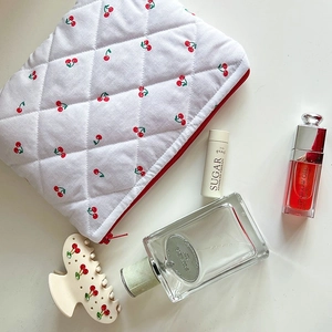 Detail of white quilted cosmetic bag with cherry print and a red zipper closure