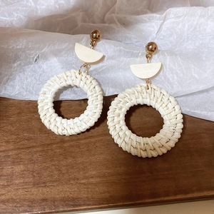 Close-up of bohemian earrings featuring natural woven straw rings and wooden accents
