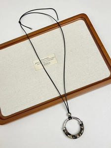 Detail view of a silver flower pendant necklace with leopard print on a linen display tray