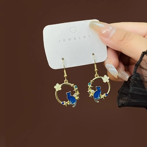 Detail of golden cat silhouette earrings with blue enamel and floral rhinestones