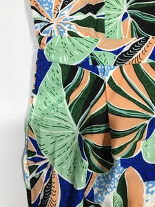 Detail of tropical print fabric with green and orange patterns on wide leg jumpsuit