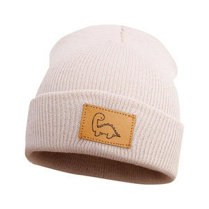 Dettaglio del berretto in maglia beige con toppa in pelle marrone e dinosauro