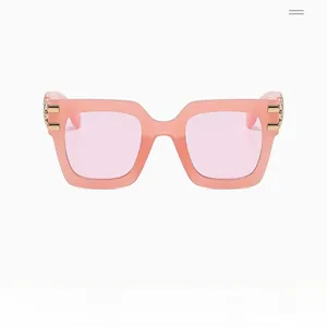 Detail of pink square sunglasses with golden metal chain accents on the temples