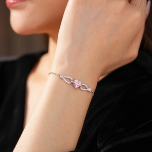Close-up of heart-shaped pink gemstone bracelet with silver chain on model wrist