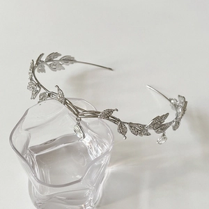 Close-up of a silver leaf bridal headband with sparkling rhinestones on a glass rim