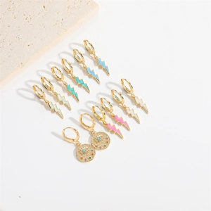 Golden lightning bolt drop earrings and evil eye studs collection on stone background