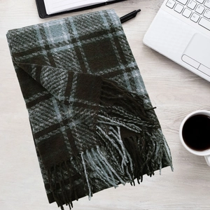 Detail of dark green plaid scarf with soft fringe on a wooden desk with a laptop