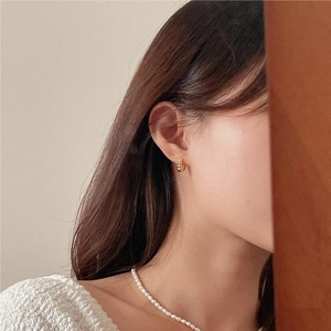 Detailed view of model wearing a gold twist earring and layered white pearl necklace