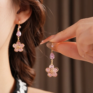 Close-up of elegant gold earrings with pink flower and teardrop zircon pendants