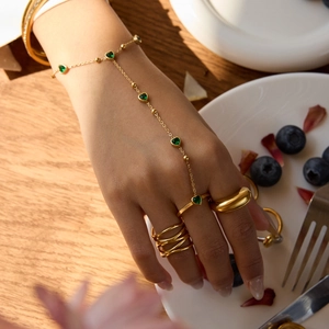 Détail d'un bracelet de doigt doré avec pierres de cœur vertes sur la main d'un mannequin