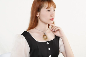 Close-up of a gold hollow circular pendant on a silver chain worn by a model