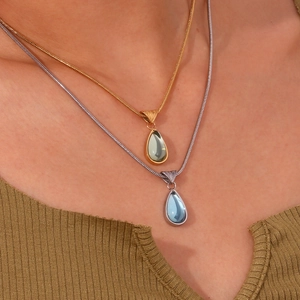Close-up of teardrop pendant necklace set with light blue and green gems on model neck