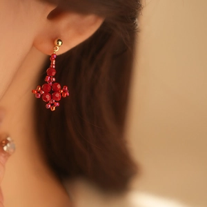 Detailed close-up of red beaded clover earrings with elegant gold metal hardware accents