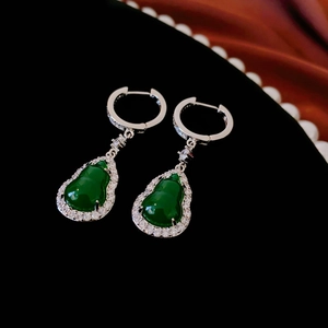 Macro view of green resin gourd earrings with zircon inlay on a dark velvet background