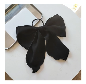 Close-up of a large black bow hair scrunchie with soft fabric on a white tabletop