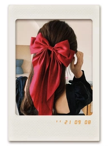 Close-up of a large red satin bow hair clip with ribbons on a female model