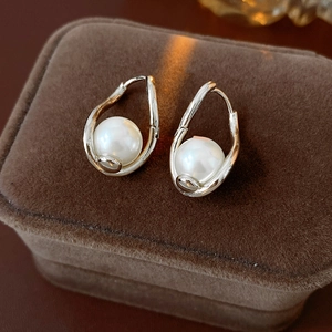 Detailed macro view of twisted silver earrings with white pearls on brown velvet tray