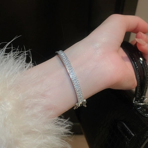 Detail of silver tennis bracelet with cubic zirconia on wrist with black leather bag