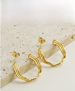 Detail view of gold C-shaped earrings with irregular wave texture on travertine stone