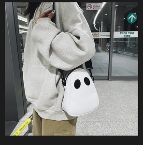 Ghost-shaped PU leather crossbody bag with black oval eyes worn by a model in an airport