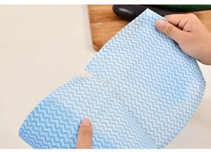 Detail showing hands tearing a disposable blue wavy print kitchen wipe with easy-tear design