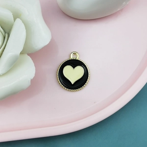 Detail of round black alloy pendant with cream heart and gold wavy edge on pink tray
