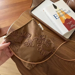 Détails de broderie sur un sac bandoulière en daim camel avec motifs floraux raffinés