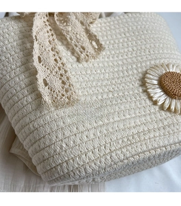 Detail of cream woven tote bag featuring delicate lace bow and 3D daisy flower accessory