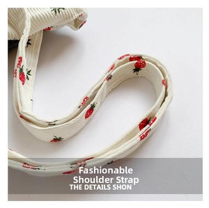 Detail of corduroy shoulder strap featuring red and green strawberry prints and soft texture