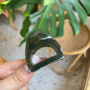 Detailed close-up of a dark green resin hair claw clip with golden metal spring