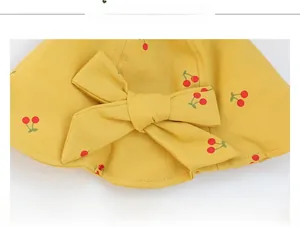 Detailed shot of yellow baby bucket hat featuring red cherry prints and a large bow tie