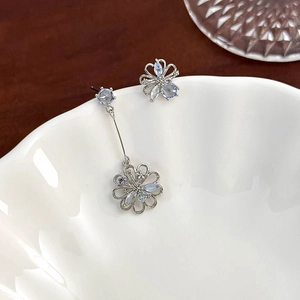 Macro shot of asymmetrical silver flower earrings with blue and purple crystals in a white bowl