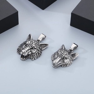 Detailed view of two vintage silver stainless steel wolf head pendants on a gray surface