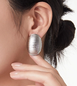 Detailed view of large silver cocoon textured metal earrings worn by a model