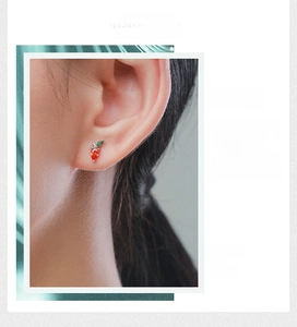 Macro shot of carrot-shaped silver stud earrings with orange and green gems on a model