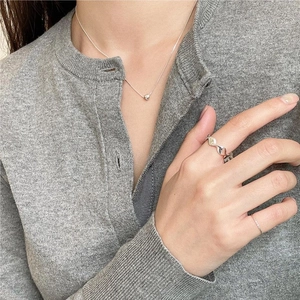 Close-up of minimalist 925 sterling silver wave ring and heart pendant necklace on model