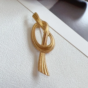 Vintage gold knot brooch with detailed woven texture on textured white surface