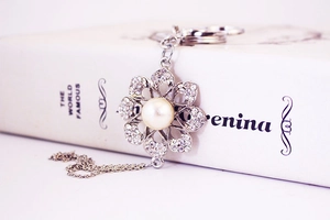Detail of silver alloy flower keychain with pearl center and crystal petals on a book