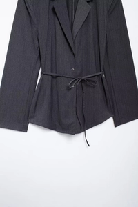 Detail of dark grey tailored blazer featuring a belted waist and three-button closure