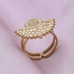 Macro shot of gold stainless steel ring with textured fan motif on purple silk fabric